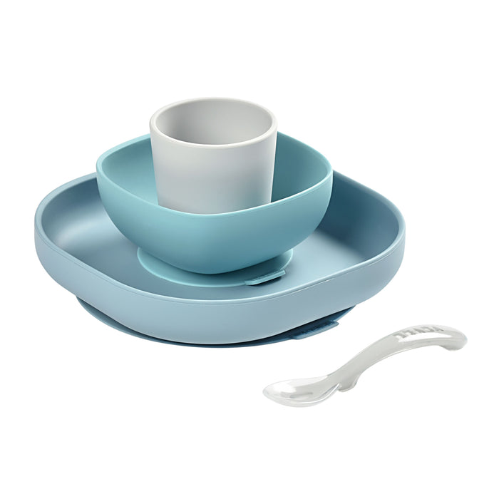 A set of blue and white childrens dishware, including a square plate, a bowl, a cup, and a spoon, all made of plastic, arranged on a white background.