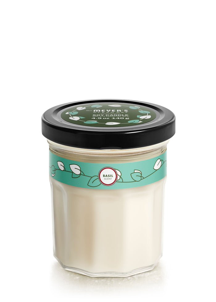 A clear glass jar with a black lid containing a white candle. The lid and label are green with white leaf designs, and Basil is written on the label.