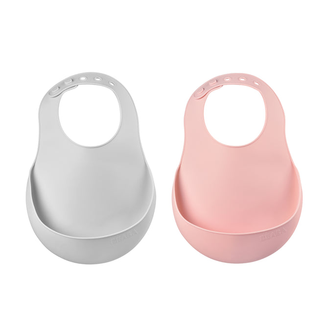 Two silicone baby bibs, one light gray and one light pink, each with an adjustable neck strap and a wide pocket at the bottom for catching food. The bibs are displayed side by side on a white background.