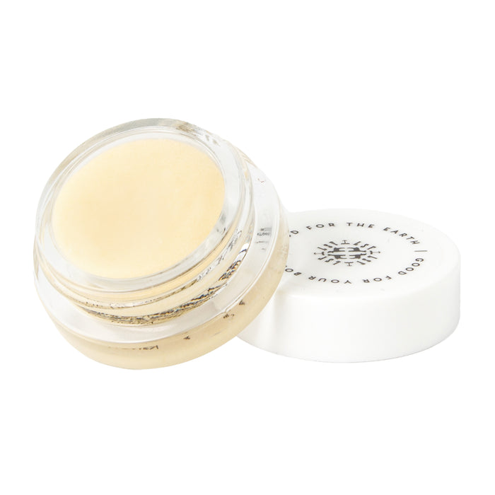 A small, clear jar of Little Seed Farm Honey Lip Treatment with a white screw-on lid set slightly aside. The lid displays black text and a central symbol, reflecting its soothing, hydrating formula for lips.