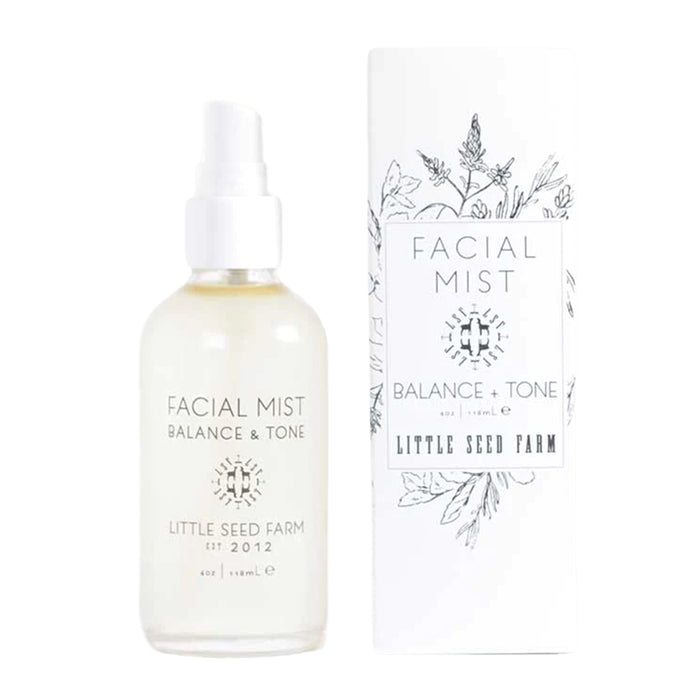 A clear glass bottle labeled Toning Facial Mist by Little Seed Farm, featuring pH balancing mist with organic aloe juice, stands beside its matching white box decorated with botanical illustrations and identical branding.