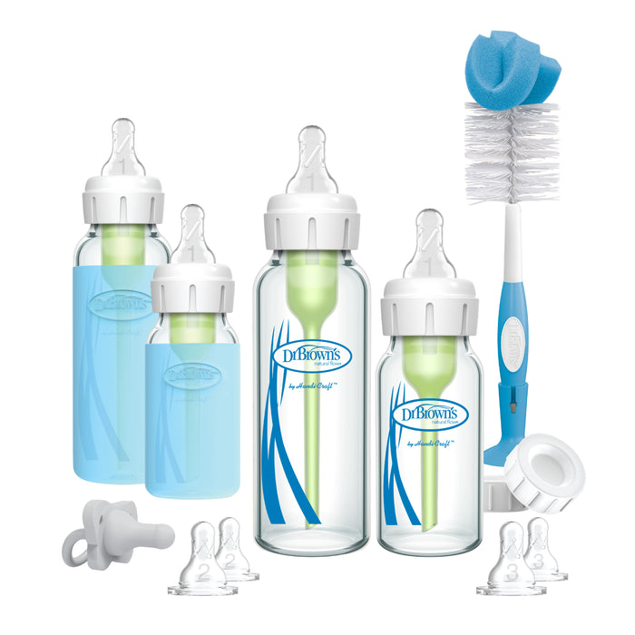 A set of Dr. Browns baby bottles with green internal vents, four clear silicone nipples, a pacifier, a blue and white bottle brush, and a white cleaning tool, all displayed on a white background.