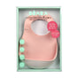 A boxed set of two BEABA silicone bibs, one pink and one white, is displayed in mint green packaging with text in French and English: Not a crumb is lost. The bibs have a food-catching pocket.