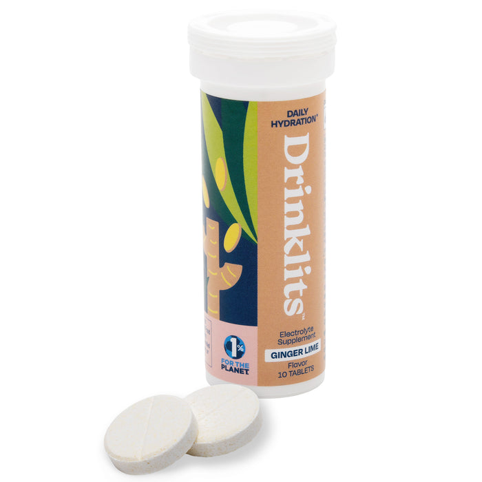 A tube labeled Drinkilts Daily Hydration, Electrolyte Supplement, Ginger Lime Flavor stands upright with two round, white tablets lying beside it. The label has ginger and lime graphics and mentions 10 tablets and 1% for the Planet.