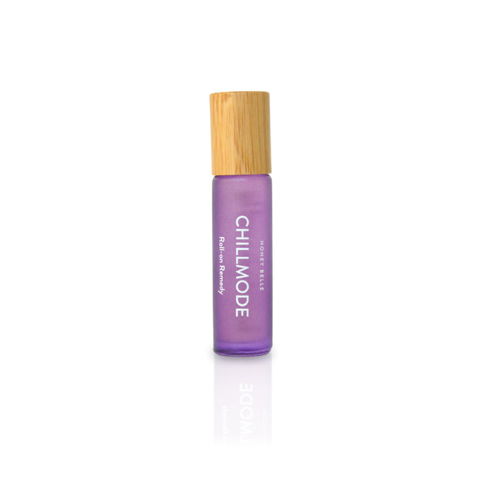 A purple glass roll-on bottle labeled CHILL MODE with a light wooden cap, standing upright on a white background. The label also reads Rooted Beings and Ritual Remedy.