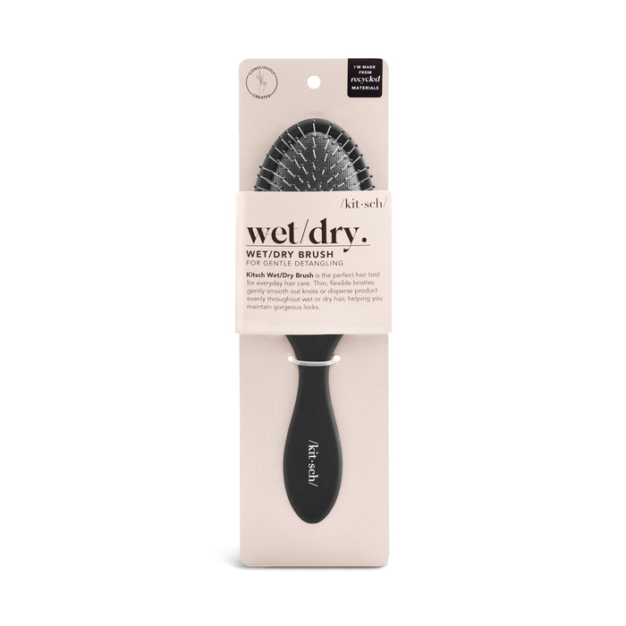 A Kit•sch wet/dry hairbrush in black with a cushioned, pin-style bristle head, displayed in beige packaging labeled “wet/dry brush for gentle detangling.”.
