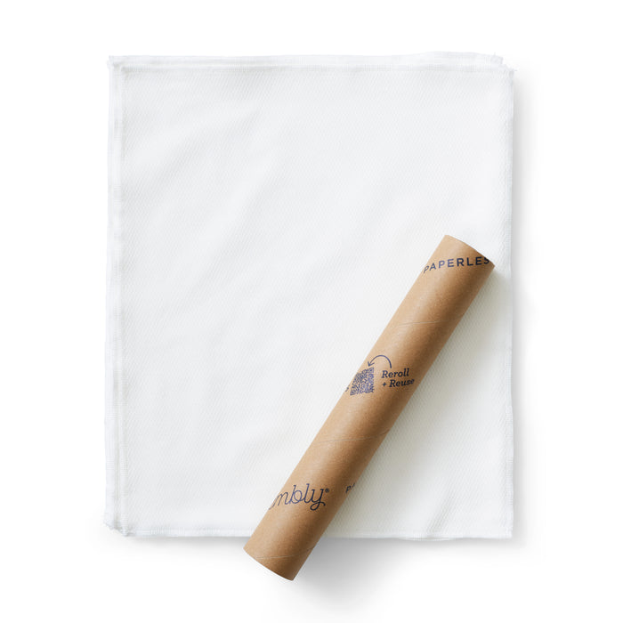 A rolled brown paper tube labeled Paperless rests on top of a neatly folded stack of white reusable cloths, set against a plain white background.