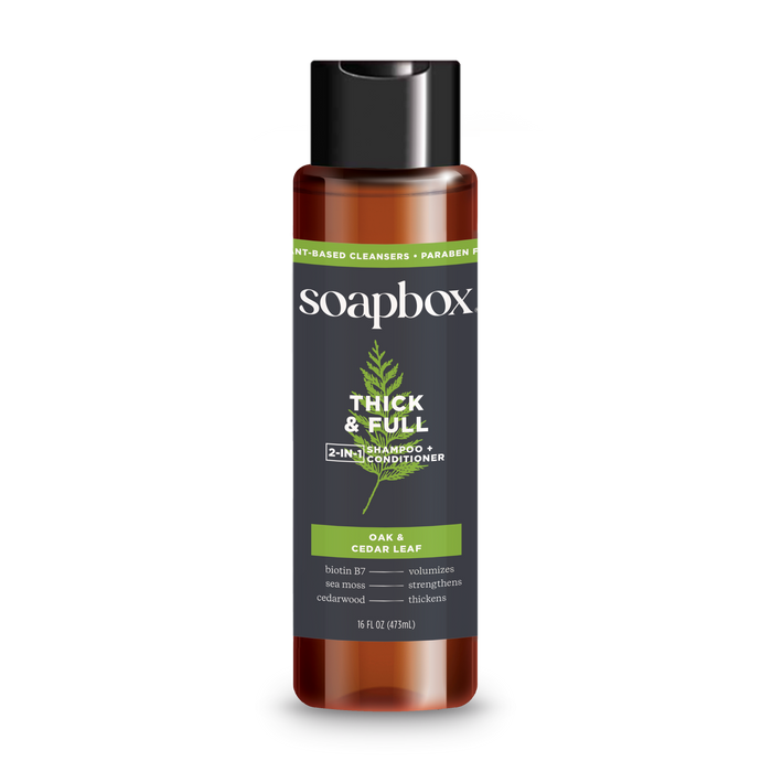 The Soapbox Thick & Full 2-in-1 Shampoo & Conditioner, infused with oak, cedar leaf, and biotin B7, volumizes and strengthens hair for a fuller look. Its packaged in a brown bottle with a black cap and green label accents.