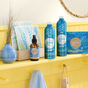 Grove Co.s vibrant spring collection, featuring a dish soap refill, hand soap, and laundry detergent sheets in bold blue and green packaging, displayed on a bright yellow shelf. Completing the arrangement are a vase and dishcloths—all crafted to combat plastic pollution.