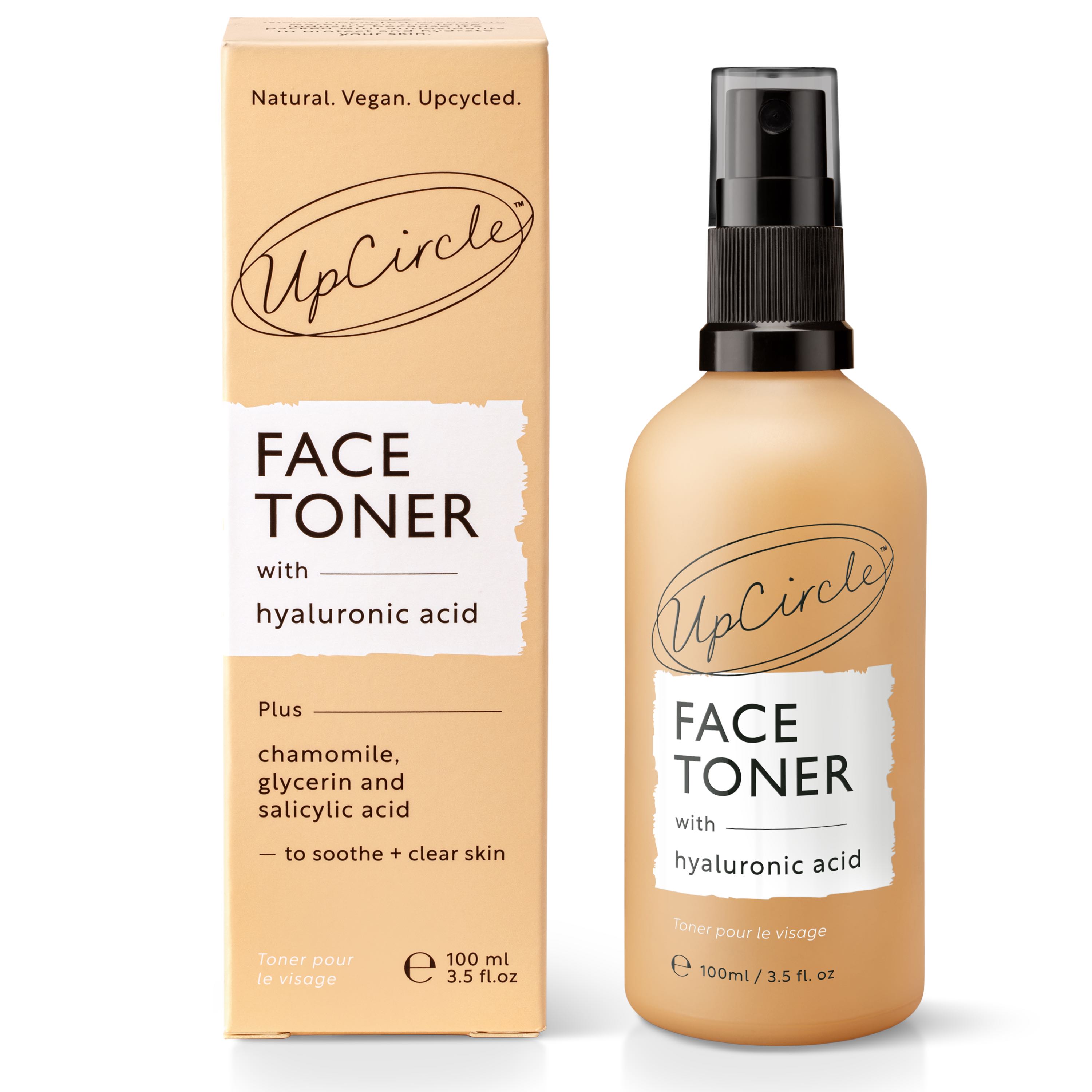An UpCircle Face Toner spray bottle with hyaluronic acid is displayed next to its matching cardboard box, highlighting natural ingredients like chamomile, glycerin, and salicylic acid. Both feature a beige design with black and white text for a hydrating experience.