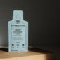 A sachet of Cymbiotika Liquid Colostrum, featuring grass-fed colostrum for immune and digestive support, stands upright on a wooden surface with a dark, blurred background. The vanilla sea salt flavor is visible on the label.