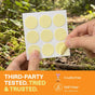 A person peels a yellow patch from a sheet outdoors. Text below reads: Third-party tested. Tried & trusted. Cruelty free. DEET-free* (*Not a safety claim). The background features green plants and fallen leaves, highlighting Cliganic Mosquito Repellent Patches – Essential Oil Infused for reliable, plant-based protection.