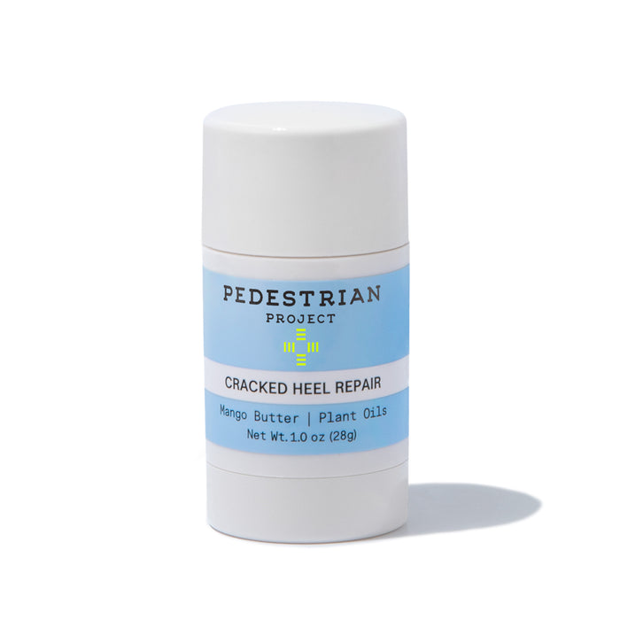 A white cylindrical stick container labeled PEDESTRIAN PROJECT CRACKED HEEL REPAIR with blue accents, featuring mango butter and plant oils, net weight 1 oz (28g), standing upright on a white background.