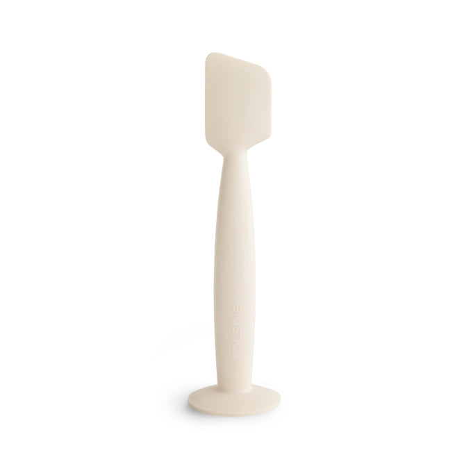 The mushie Diaper Cream Applicator is a white, food-grade silicone tool with a flat, rectangular head and curved handle on a wide base—keeping diaper cream application soft, mess-free, and baby essentials organized.