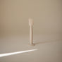 A minimalist beige mushie Diaper Cream Applicator made from BPA-free soft silicone stands upright on a smooth, light-colored surface under soft lighting, casting a gentle shadow to the right.