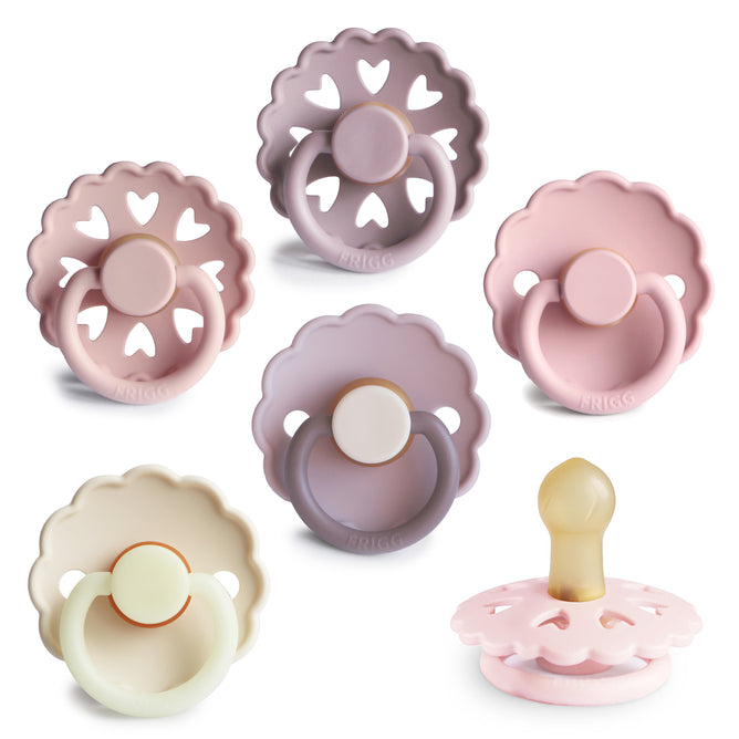 Six mushie FRIGG Natural Rubber Pacifiers (BPA-Free 6-Pack) in pastel pink, purple, and beige feature scalloped-edge shields with heart cutouts and a Click-lock® system; one pacifier is shown from the side.