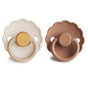 Two mushie FRIGG Daisy Natural Rubber Pacifiers—one cream with yellow center, one light brown with tan center—both BPA-free, scalloped edges, and round handles, shown side by side on a white background.