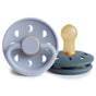 Two FRIGG Daisy Natural Rubber Pacifiers from mushie—one upright to show the BPA-free nipple, the other flat with ventilation holes and brand name—combine style and comfort for your baby in grey and beige.