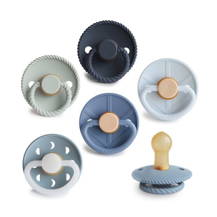 A set of six mushie FRIGG Natural Rubber Pacifiers (BPA-free, baby safe, 0-6 months) in blue, green, and gray shades, each with a round shield and beige nipple, arranged on a white background.
