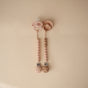 The mushie Silicone Pacifier Clip | Hera and a wooden-beaded pacifier clip, both in pink and displayed on a beige background, are essential baby accessories.