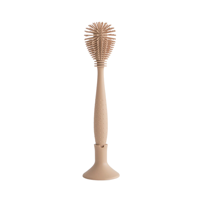The mushie Silicone Baby Bottle Brush – Dual-Head, Non-Scratch, BPA-Free in beige features a round silicone head and ergonomic handle, standing upright on a matching wide circular base.