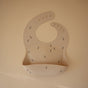 A beige mushie Silicone Baby Bib – Adjustable, featuring a front pocket and small bee designs, made from FDA-tested food-grade silicone, is displayed flat on a matching beige background.