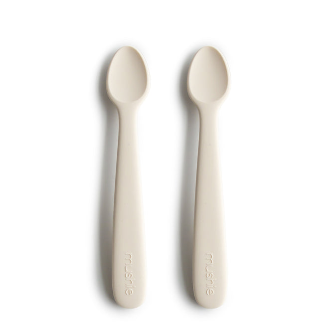 Two BPA-free, food-grade silicone feeding spoons by mushie with rounded tips and embossed handles are placed side by side on a white background.