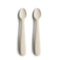 Two BPA-free, food-grade silicone feeding spoons by mushie with rounded tips and embossed handles are placed side by side on a white background.