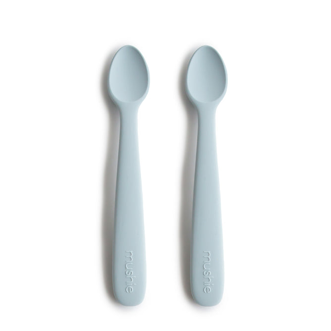 Two mushie Silicone Feeding Spoons, made from BPA-free, food-grade material, in light blue with rounded tips, lie side by side on a white background. “mushie” is embossed on the handles—perfect essentials for baby mealtime.