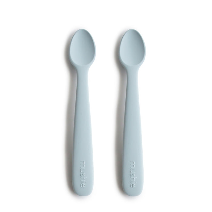 Two mushie Silicone Feeding Spoons, made from BPA-free, food-grade material, in light blue with rounded tips, lie side by side on a white background. “mushie” is embossed on the handles—perfect essentials for baby mealtime.