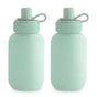 Two light green mushie Silicone Puree Pouches made from BPA-free, food-grade silicone with rounded shapes, matching caps, and loop handles are shown side by side on a white background.