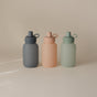 Three mushie Silicone Puree Pouches—reusable, BPA-free, and made from food-grade silicone—are shown in muted gray, peach, and light green hues with matching lids and loop handles on a neutral background.