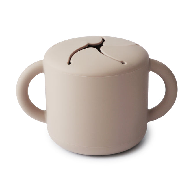 The mushie Silicone Snack Cup – Easy-Grip Handles, BPA-Free features a beige design with two handles and a spill-proof lid with flexible slits, offering convenient, mess-free snacking for young children.