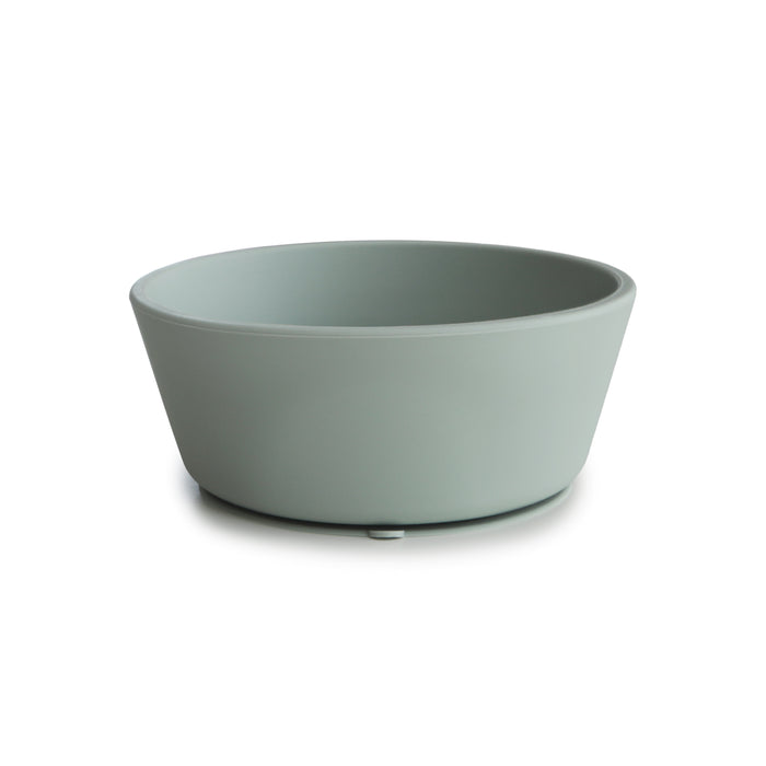 The mushie Silicone Suction Bowl, shown in light gray-green with a round, shallow shape and matte finish, is BPA-free and made from food-grade silicone. Its slightly sloped sides and small base make it a safe, non-toxic baby essential.