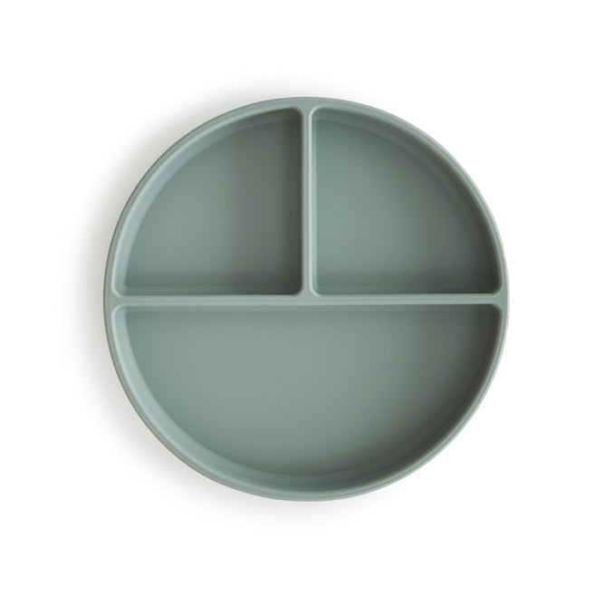 The mushie Silicone Suction Plate, made from BPA-free, food-grade silicone, features a round light green design with three compartments—two small sections on top and a larger one below—shown from above on a white background.