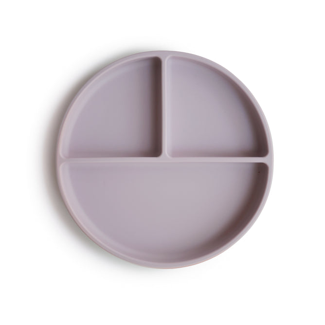 The mushie Silicone Suction Plate is a round, lavender, BPA-free, food-grade silicone plate with three Y-shaped compartments. Safe and non-toxic—ideal for baby essentials. Photographed on a white background.