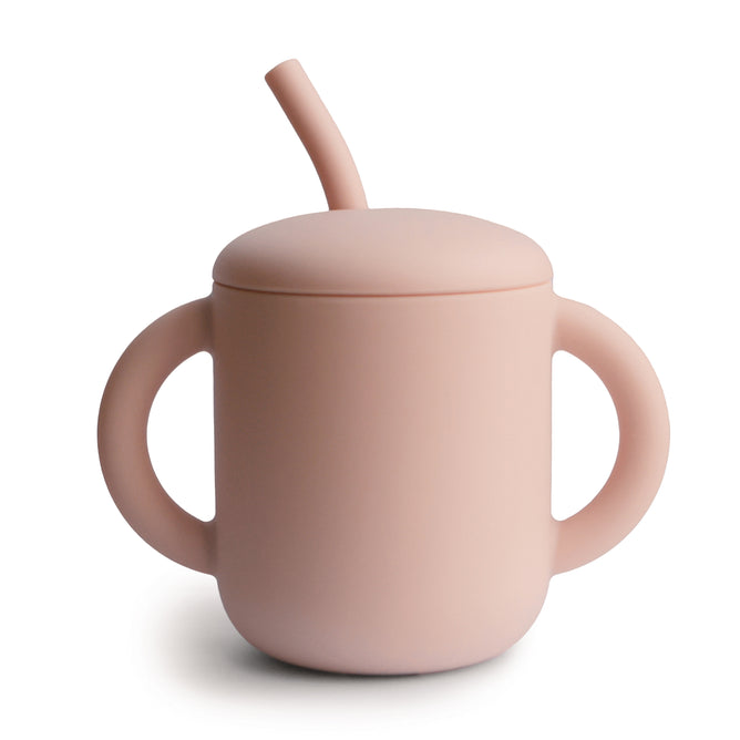 The mushie Silicone Training Cup with Straw is BPA-free and easy to hold, featuring two handles, a matching lid, and bent straw for toddlers; shown here in pink on a white background.