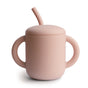 The mushie Silicone Training Cup with Straw is BPA-free and easy to hold, featuring two handles, a matching lid, and bent straw for toddlers; shown here in pink on a white background.