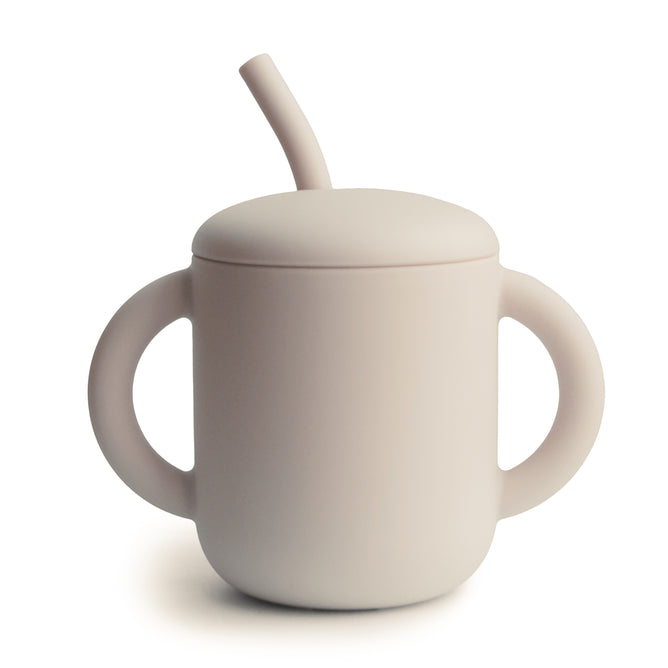 The mushie Silicone Training Cup with Straw is a beige, matte-finish, BPA-free cup made from food-grade silicone with two large handles and a built-in angled straw—perfect for baby essentials.