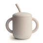 The mushie Silicone Training Cup with Straw is a beige, matte-finish, BPA-free cup made from food-grade silicone with two large handles and a built-in angled straw—perfect for baby essentials.