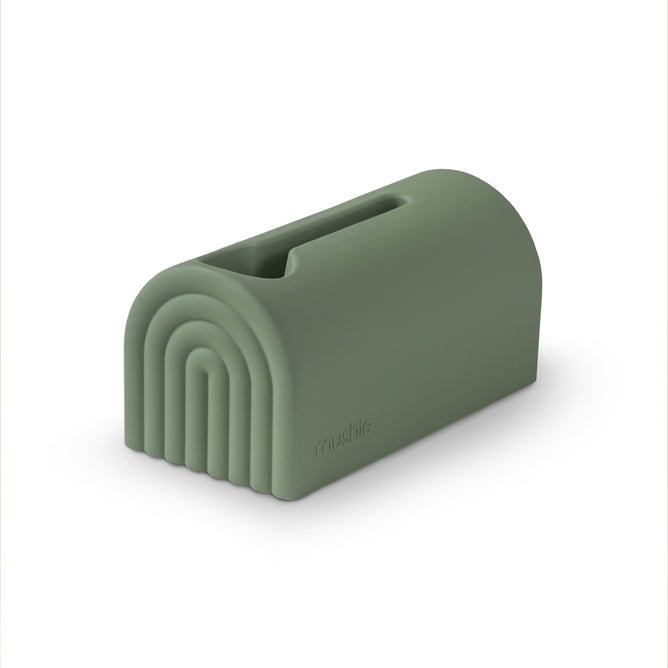 The mushie Bath Spout Cover – Soft Silicone is a green, rainbow-shaped silicone holder with a top slot for wipes or tissues, shown on a white background.