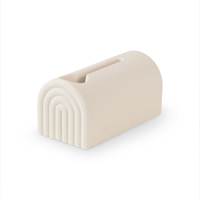 The mushie Bath Spout Cover – Soft Silicone is a beige, rectangular silicone cover with rounded edges, a rainbow arch design, and a top slot—ideal for bath time safety and shown against a white background.