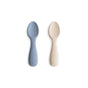 Two mushie Silicone Toddler Starter Spoons—one light blue, one beige—made from BPA-free, food-grade silicone, lie side by side on a white background. Each handle features the mushie logo embossed for a stylish touch.