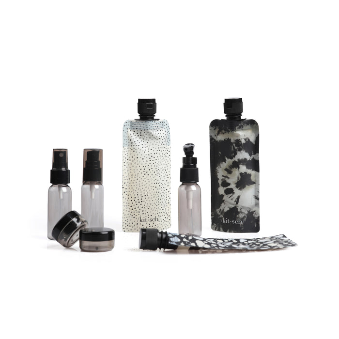 A set of reusable travel containers, including spray bottles, jars, and patterned squeeze pouches, displayed on a white background. The pouches have black and white designs.