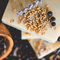 Close-up of a Chagrin Valley Soap & Salve Natural Shampoo Bar, topped with dried lavender, fenugreek seeds, and juniper berries. Made with nourishing coconut oil; another bar is visible below among scattered seeds and berries.