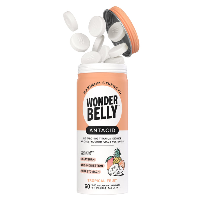 An open bottle of Wonderbelly Antacid Tropical Fruit chewable tablets with several white tablets floating above it. The label highlights relief for heartburn, acid indigestion, and sour stomach.