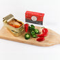 Two opened tins and a box of Natural Catch Tuna - Spicy Yellowfin Filets in Extra Virgin Olive Oil, with whole and sliced red and green chili peppers, arranged on a wooden board against a white background.