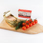 An open can of Natural Catch Tuna - Yellowfin in Olive Oil, cherry tomatoes, and dill rest on a wooden cutting board with a Natural Catch box in the background, showcasing its high protein benefits.