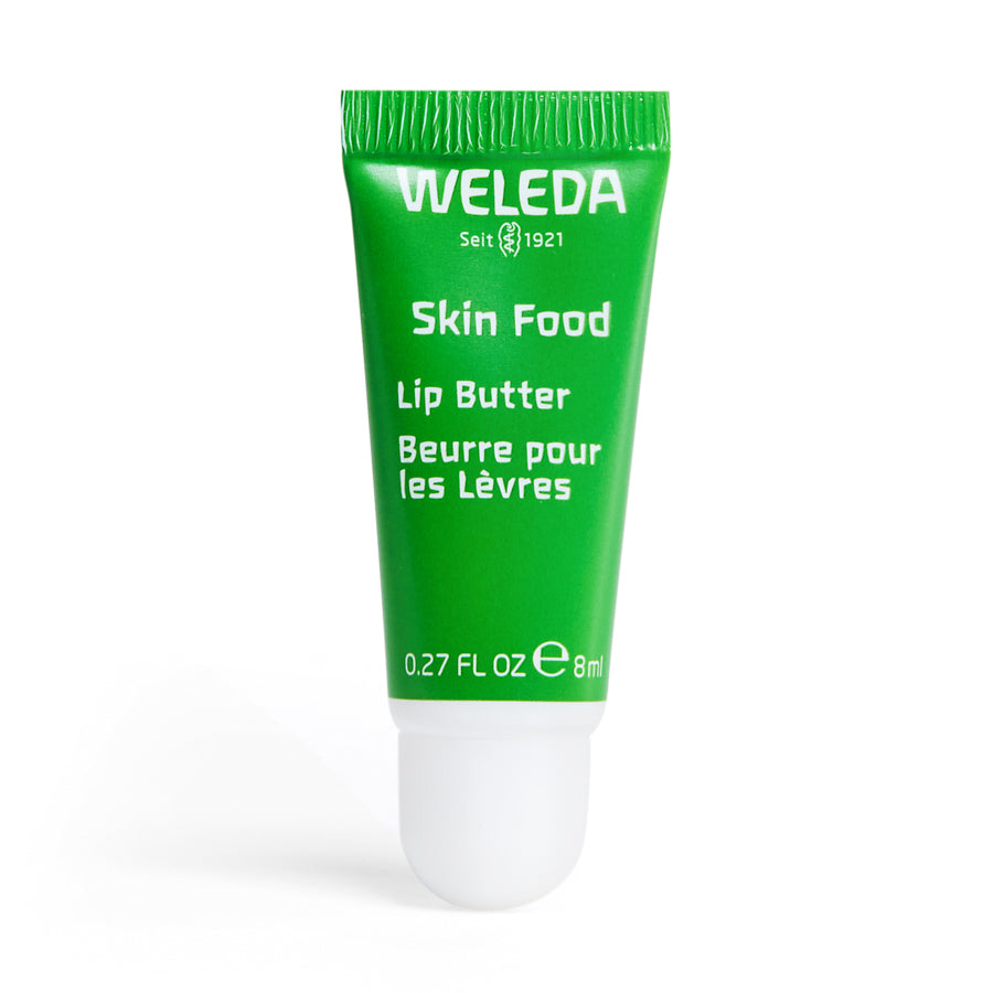 Weledas Skin Food Lip Butter, in a green tube and labeled in English and French, offers 0.27 fl oz (8 ml) of eco-friendly skincare. Featuring the Weleda logo with Seit 1921, this nourishing, natural lip product enhances beauty and sustainability.