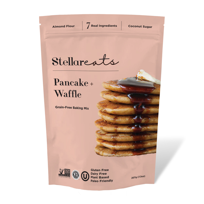 A pink pouch labeled Stellareats Pancake + Waffle Grain-Free Baking Mix features a stack of pancakes with syrup and butter. The packaging notes Almond Flour, 7 Real Ingredients, and Coconut Sugar.